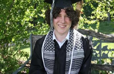 Guy Christensen smiling on his graduation day wearing a cap and gown, celebrating his academic achievement.