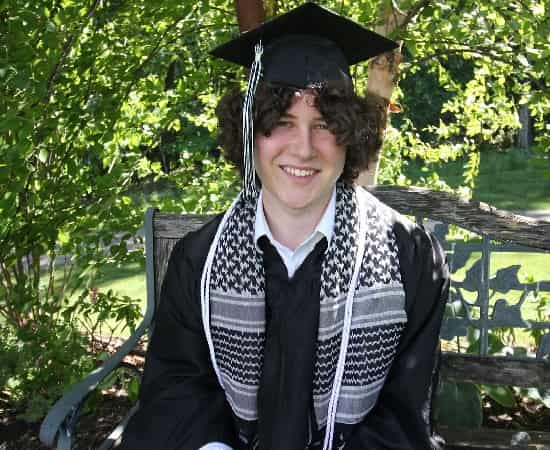 Guy Christensen smiling on his graduation day wearing a cap and gown, celebrating his academic achievement.