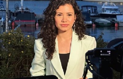 Laura Barrón-López reporting outdoors with boats in the background, wearing a light blazer.