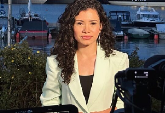 Laura Barrón-López reporting outdoors with boats in the background, wearing a light blazer.