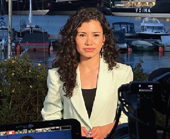 Laura Barrón-López reporting outdoors with boats in the background, wearing a light blazer.